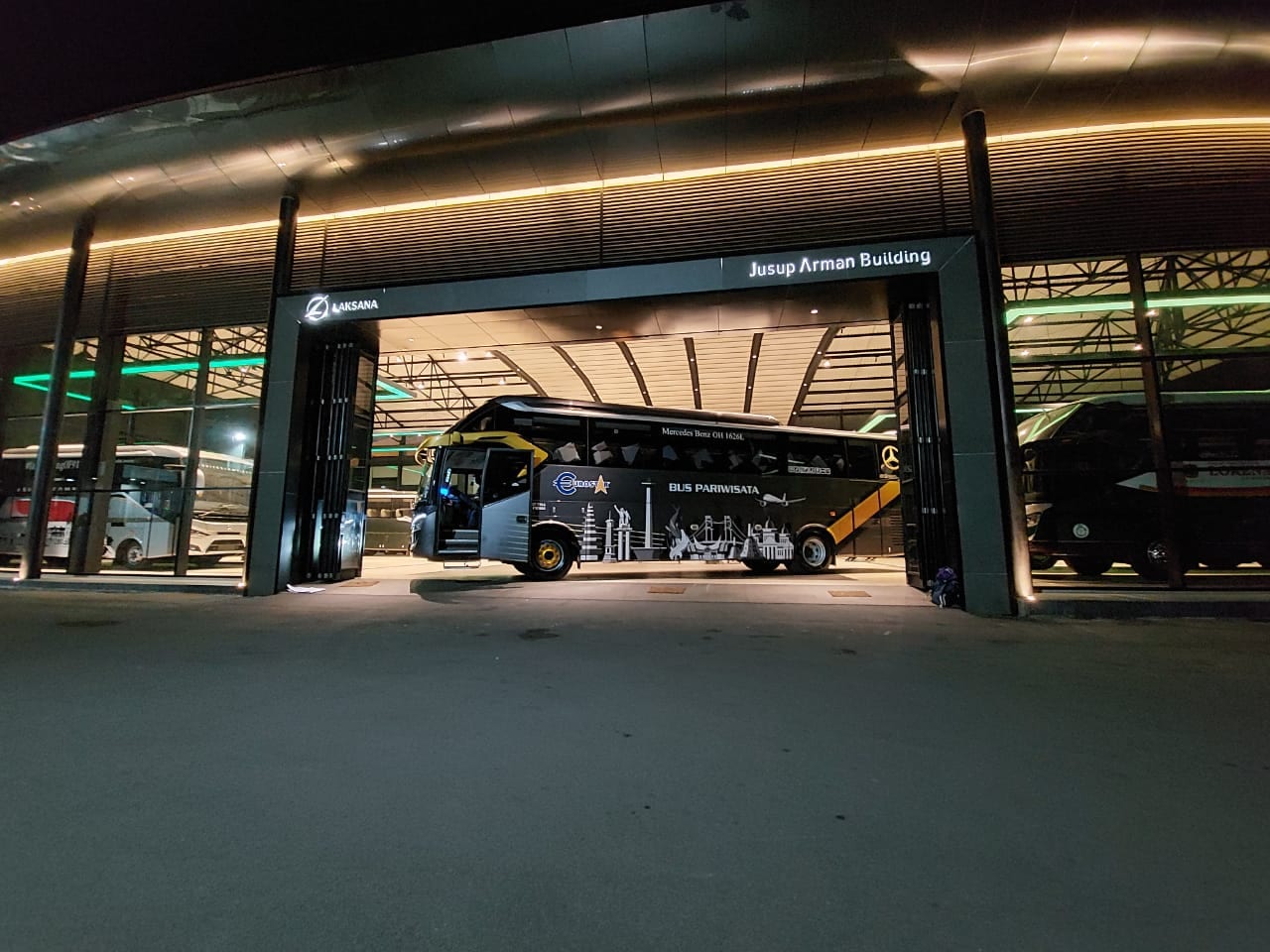 Bus Cona Hede terparkir di dalam gedung karoseri pada malam hari dengan pencahayaan hangat