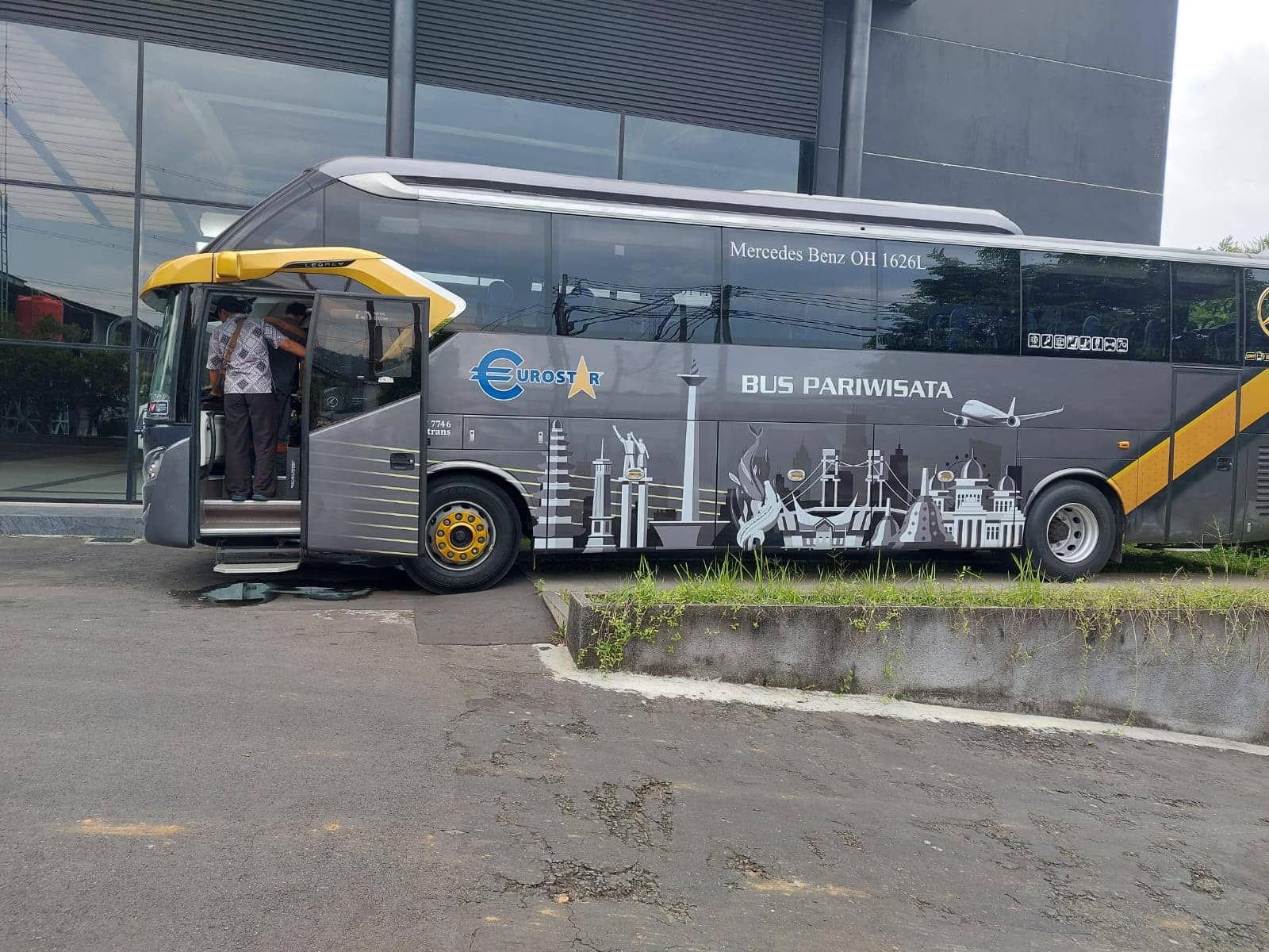 Sisi kiri bus Cona Hede dengan pintu penumpang terbuka dan ilustrasi ikon kota pada badan bus
