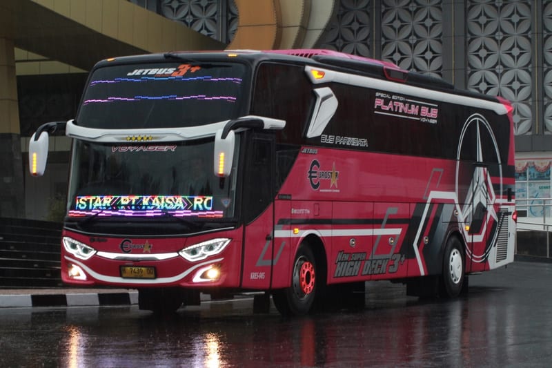 Bus pariwisata Platinum Bus berwarna merah bertuliskan Platinum Bus dengan lampu depan menyala, tampak samping depan