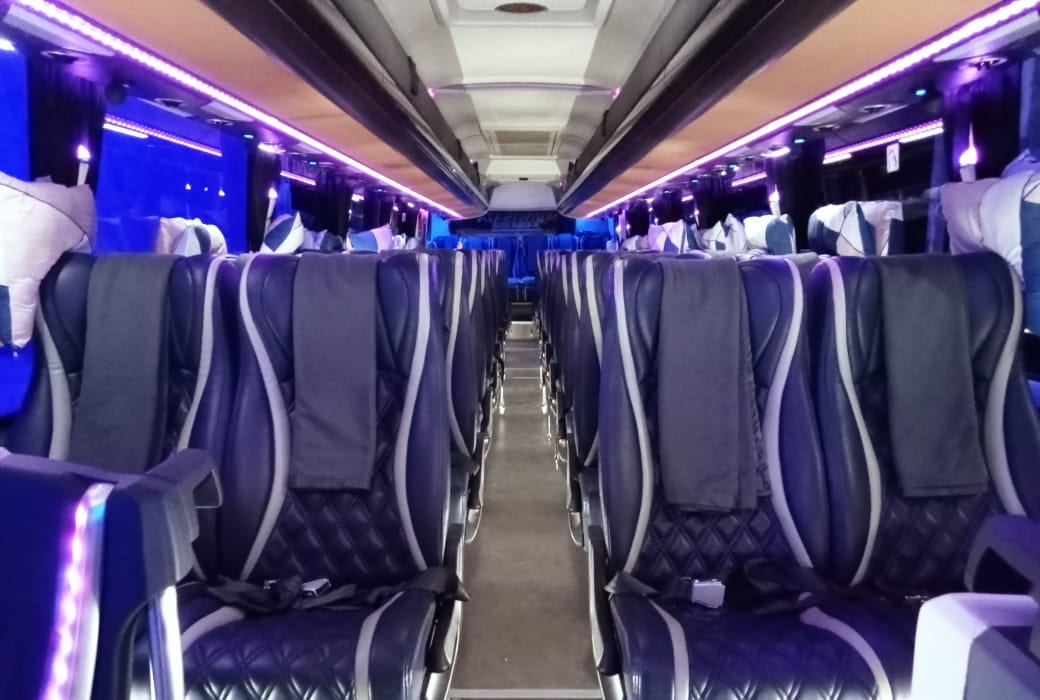 Kursi biru bermotif jahitan wajik dengan selimut dan bantal untuk setiap penumpang, diterangi lampu kabin ungu